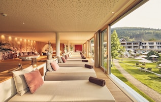 Un área de spa con varias camillas de masaje dispuestas en fila, un mostrador de recepción y vistas del hotel y el paisaje circundante.