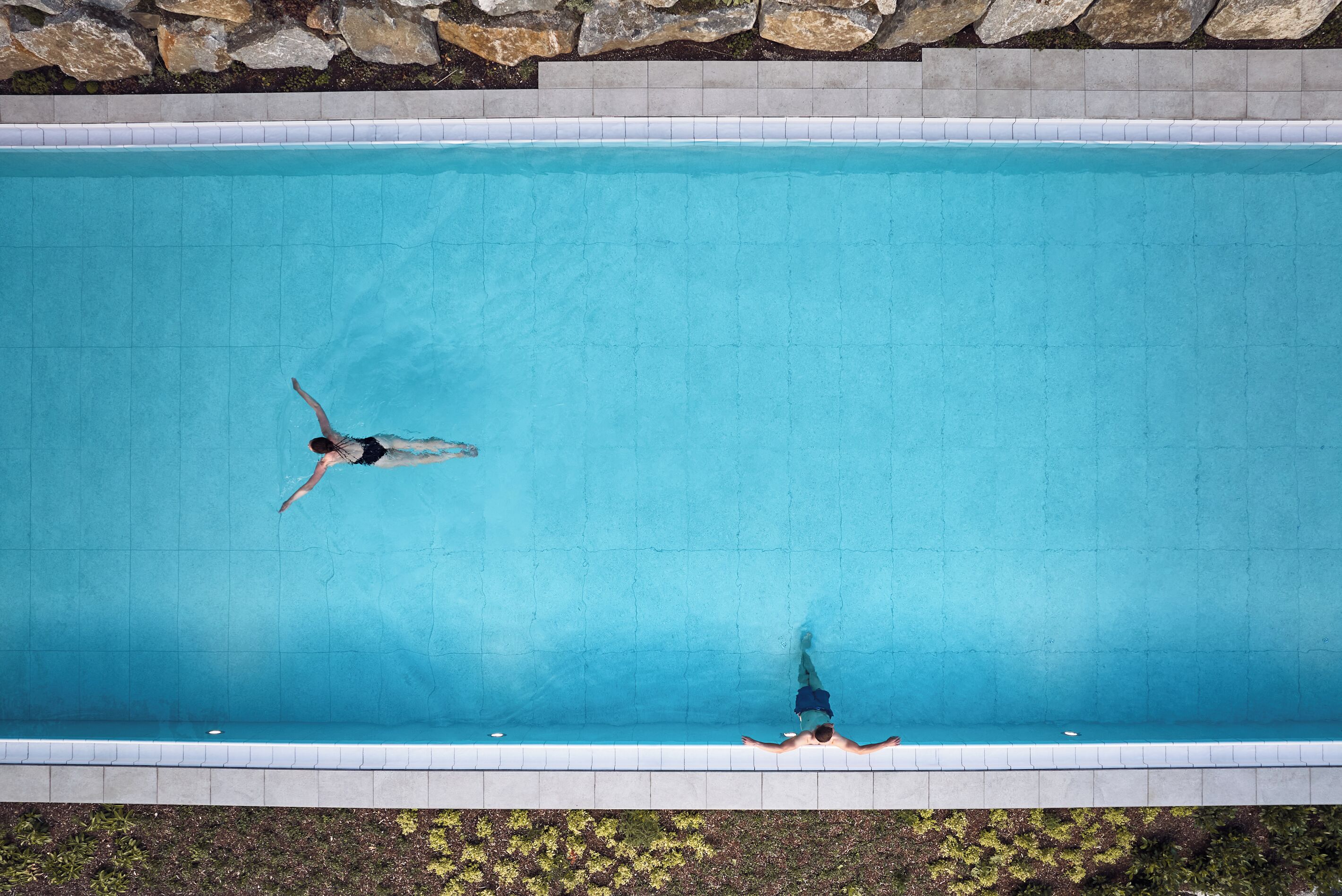 Vue aérienne d’une piscine rectangulaire dont les bords sont recouverts de carreaux et qui est bordée de pierres sur sa partie supérieure.