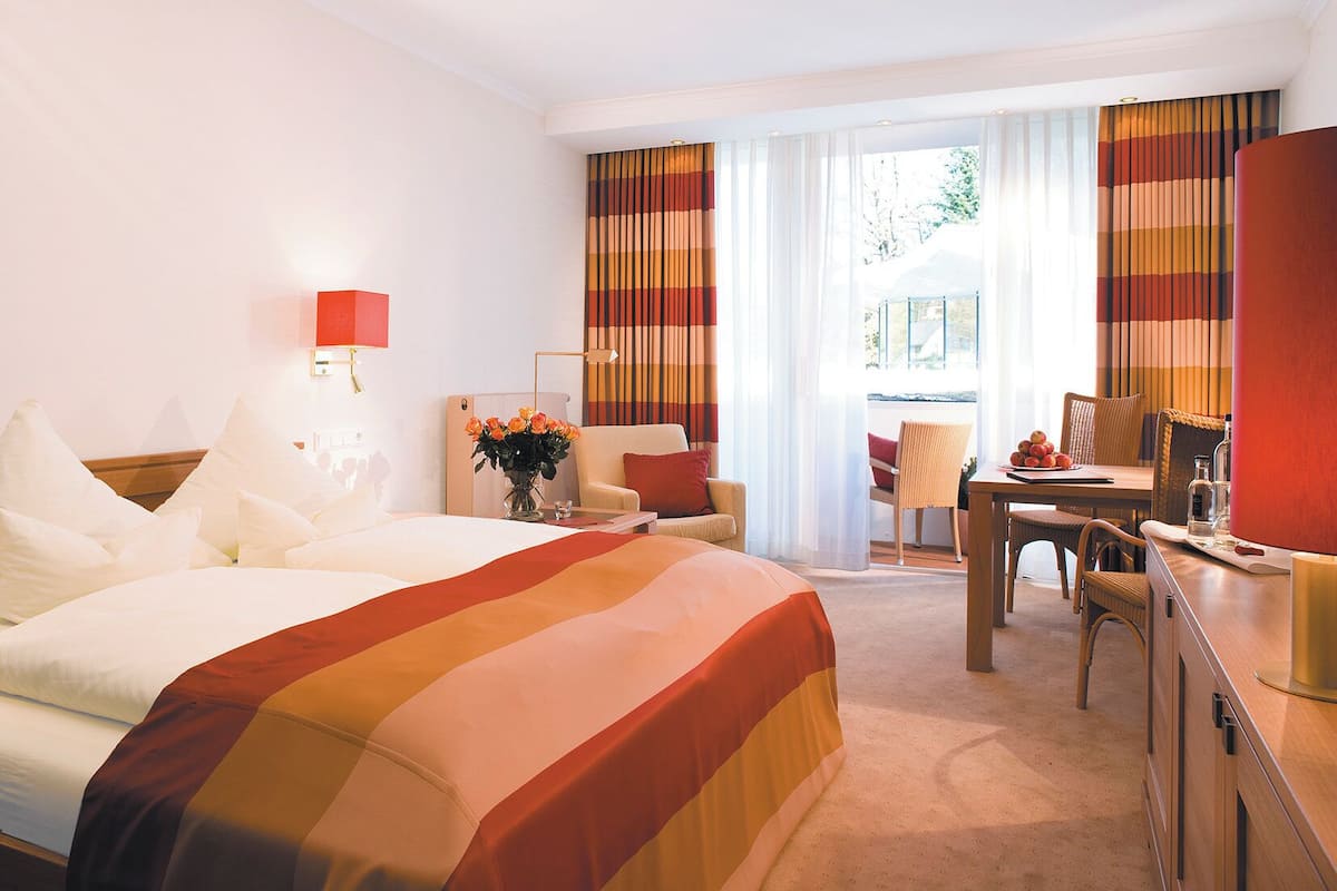 A hotel room with a large bed, a desk, a chair, and a view of the outdoors.
