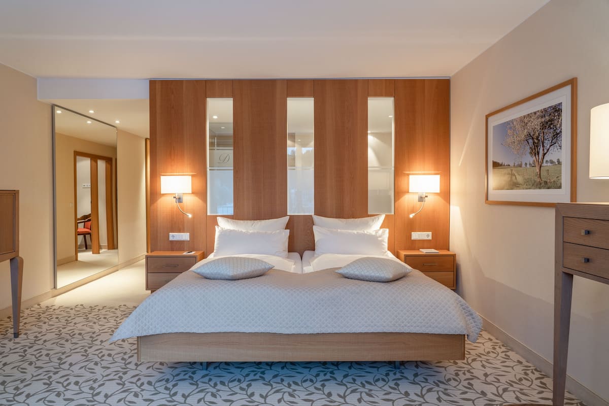 A modern hotel room with a large bed, wooden headboard, two bedside lamps, a mirror, and a framed picture on the wall.