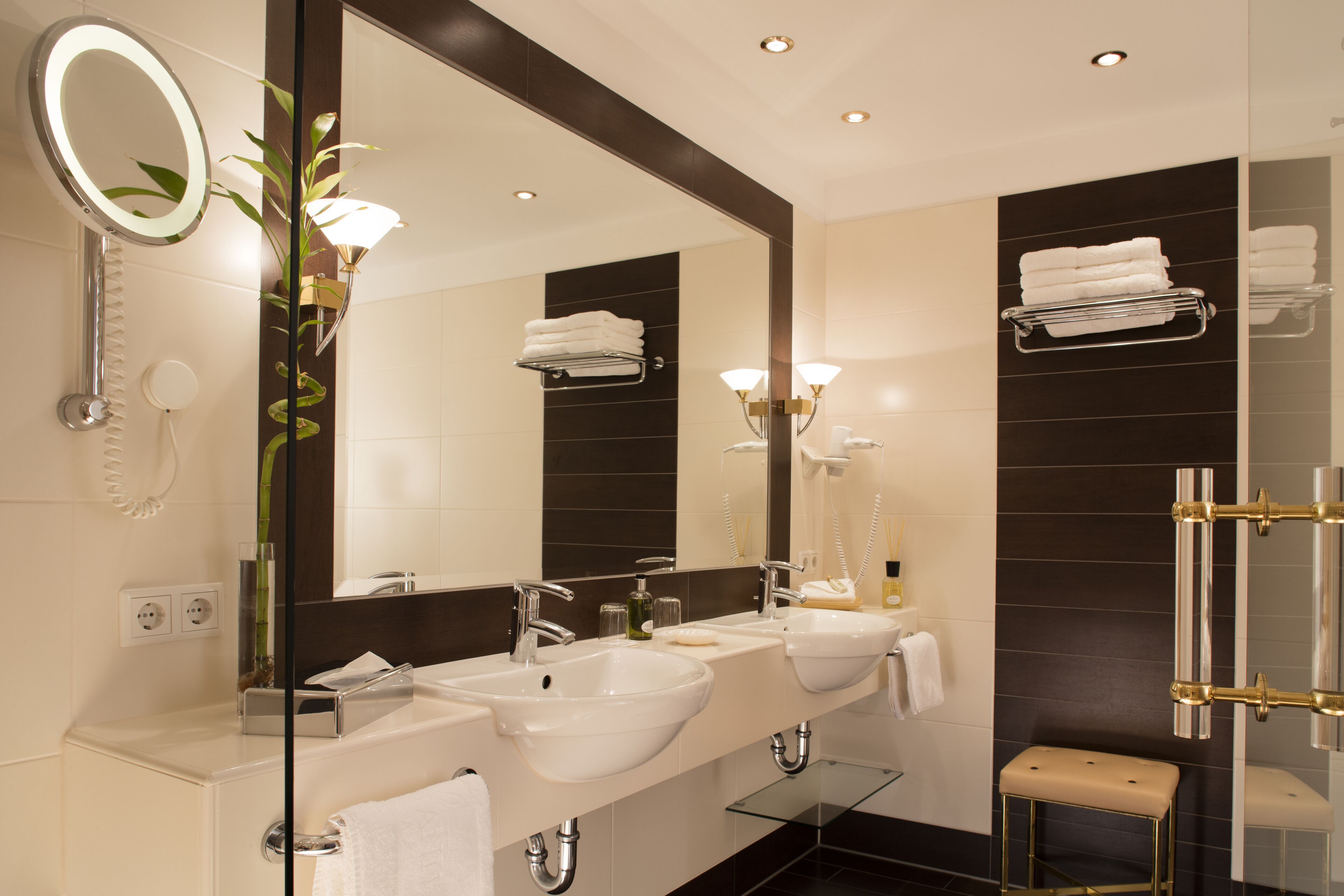 Un baño moderno con dos lavamanos, un espejo grande, un banco de vidrio y un perchero para toallas.
