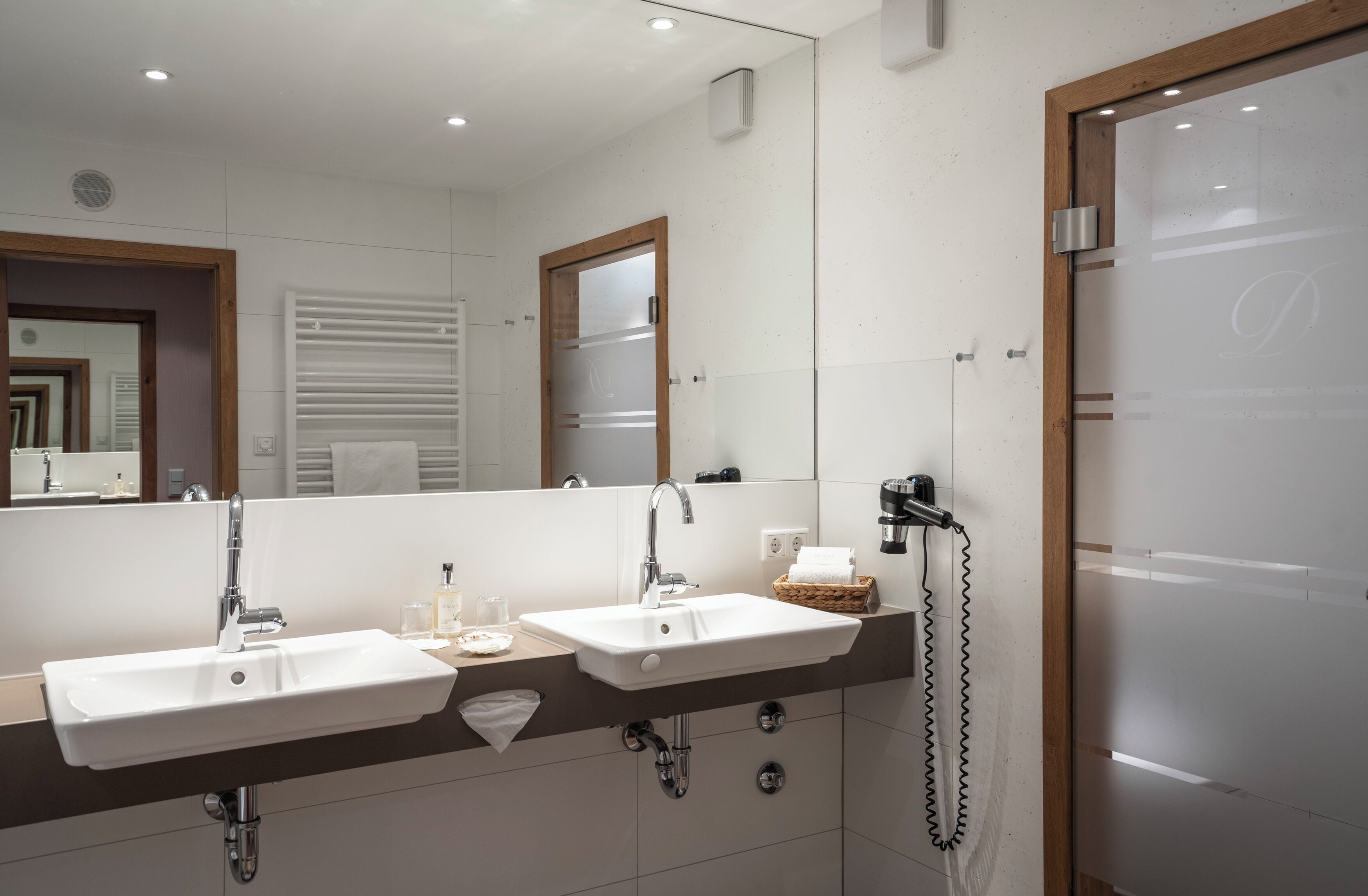 A modern bathroom with two sinks, a large mirror, and a hairdryer on a stand.