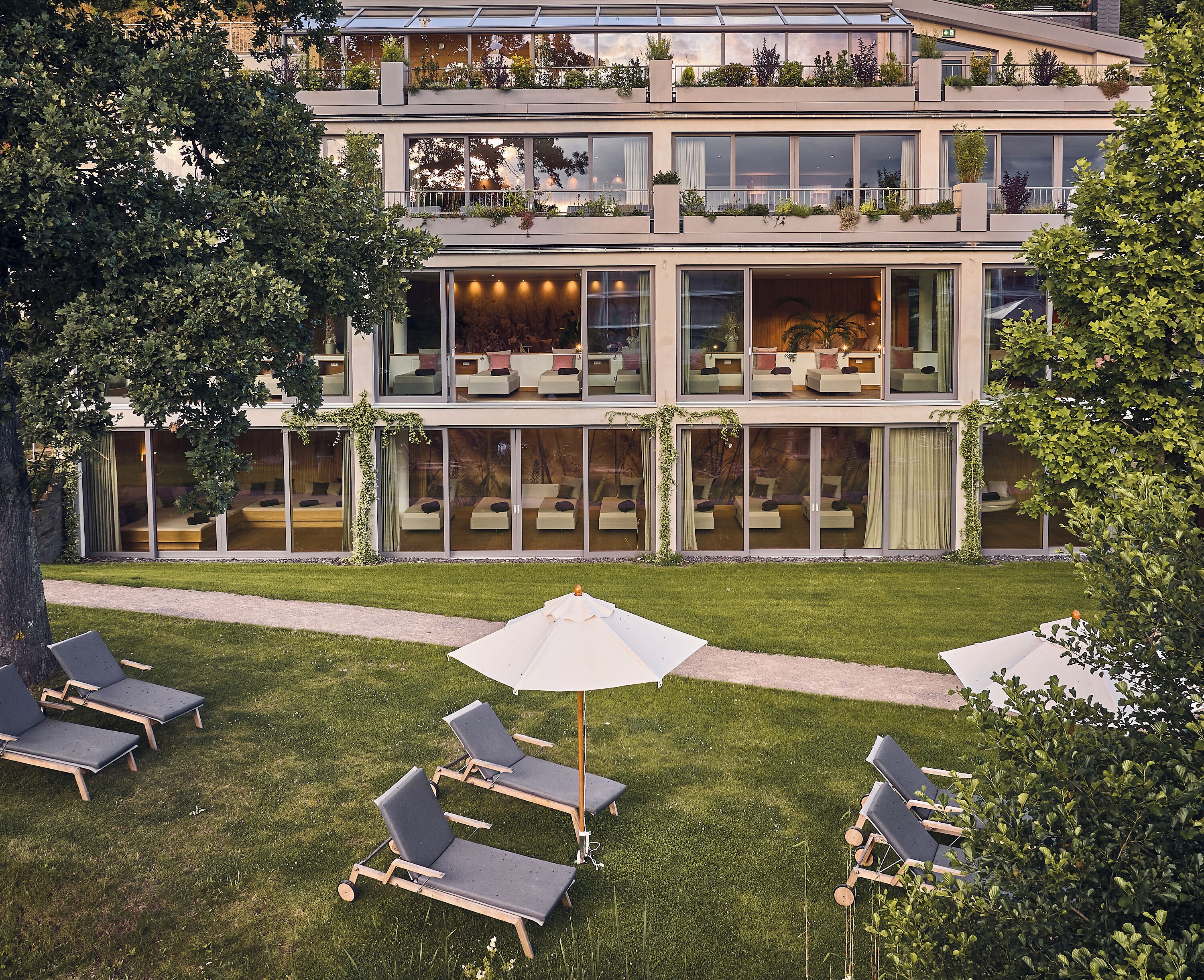 A modern multi-story building with large windows, outdoor seating, and greenery.