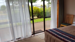 A room with a bed, a chair, and a view through a glass door to a garden and buildings. - Ace Motor Lodge (Rotorua)