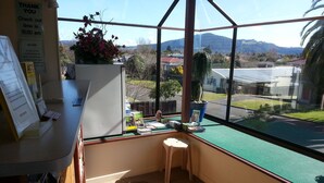 A small office with a desk, a chair, and a view of a residential area with houses and mountains. - Ace Motor Lodge (Rotorua)