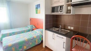 Een compacte kamer met kitchenette, twee bedden met kleurrijk beddengoed en een houten vloer.
