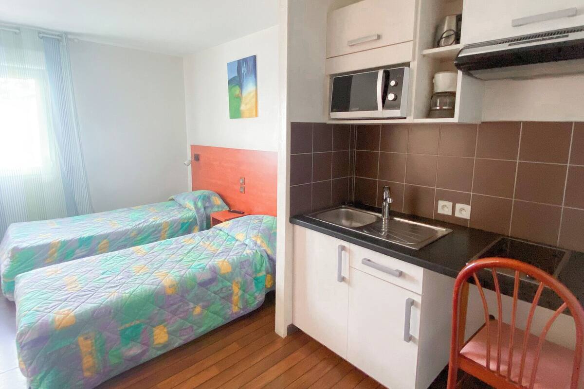 Una habitación compacta con kitchenette, dos camas con ropa de cama colorida y suelo de madera.