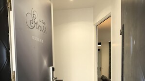 Un pasillo con una puerta negra a la izquierda, una pared blanca y suelo de madera.