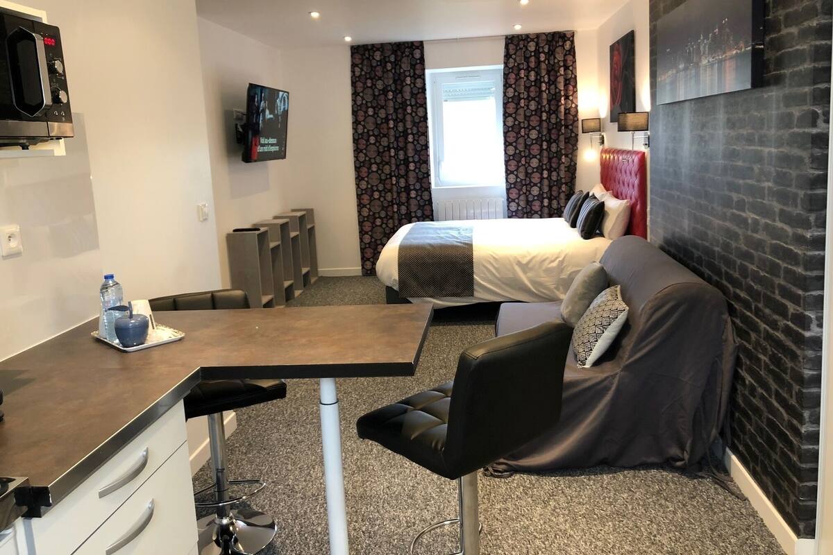 A hotel room with a bed, a desk, a chair, a TV, and a window with curtains.