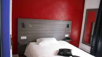A hotel room with a red wall, a grey headboard, a white bed, a bedside table with a phone, and a mirror.