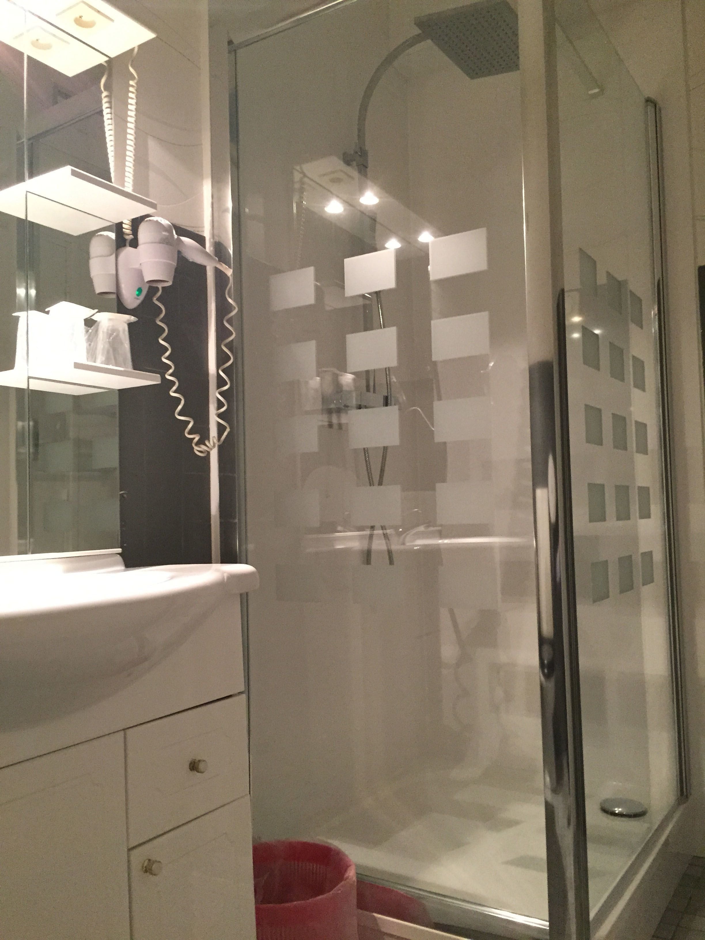 A modern bathroom with a glass shower enclosure, a white sink with a mirror above it, and a red trash bin.