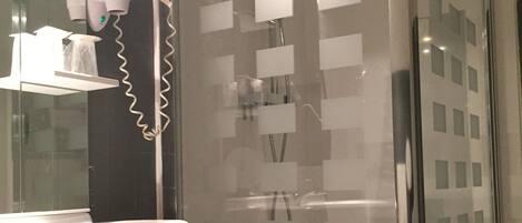 A modern bathroom with a glass shower enclosure, a white sink with a mirror above it, and a red trash bin.
