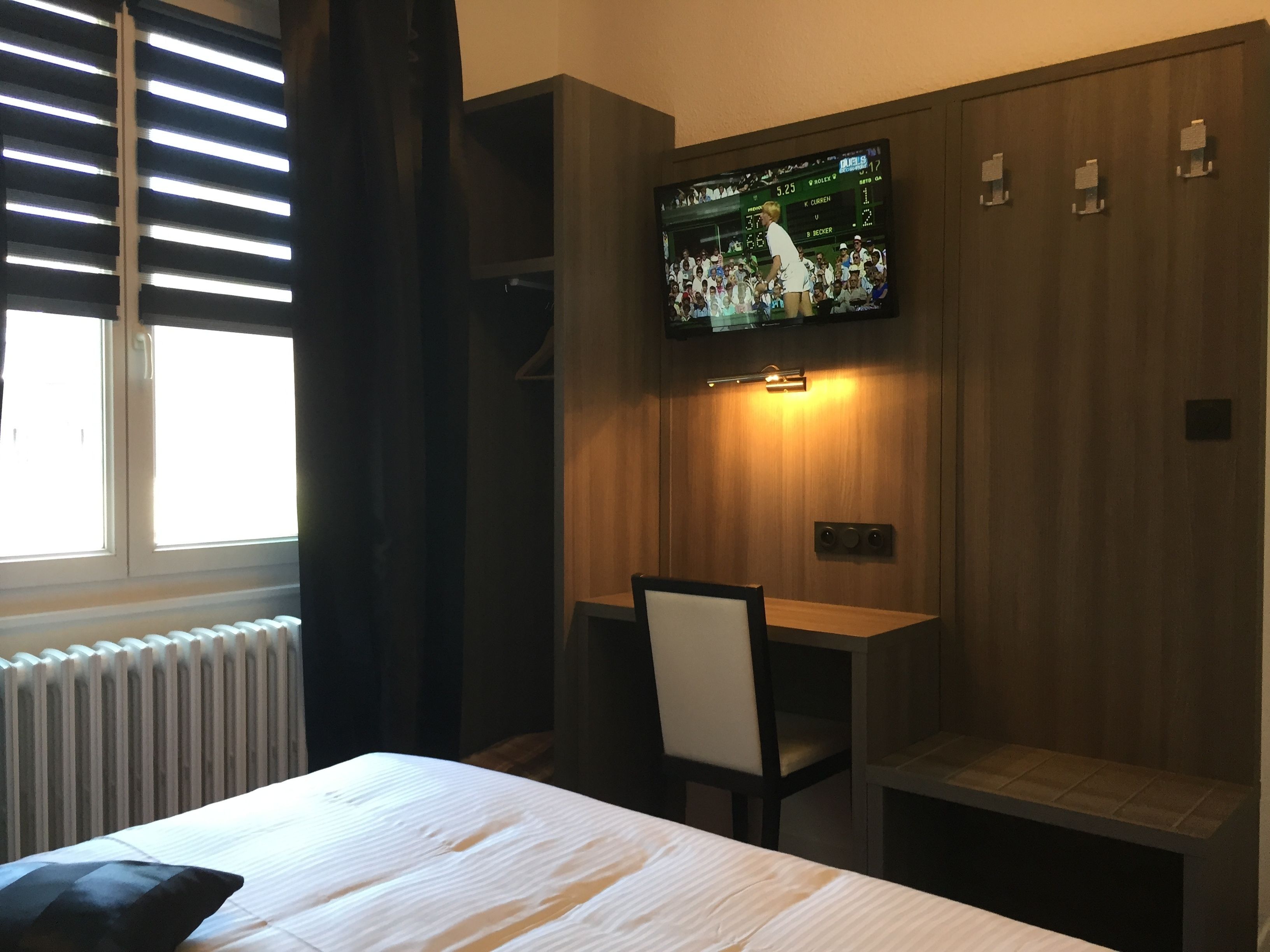 Une chambre d’hôtel équipée d’un lit, d’un bureau et d’un téléviseur fixé au mur, qui diffuse un événement sportif.