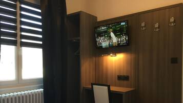 Una habitación de hotel con una cama, un escritorio y un televisor montado en la pared mostrando un evento deportivo.