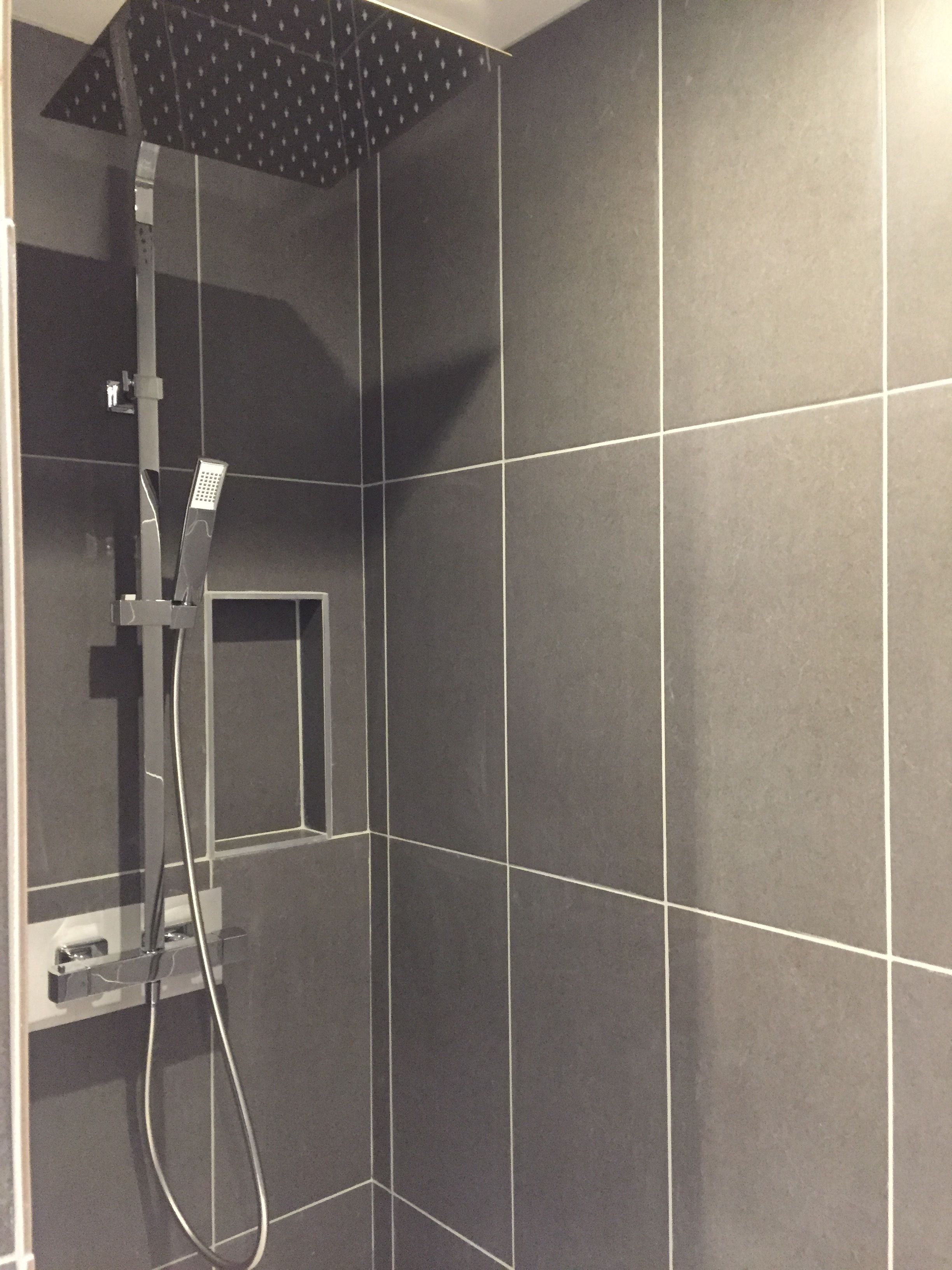 A shower area with dark tiles and a modern showerhead.