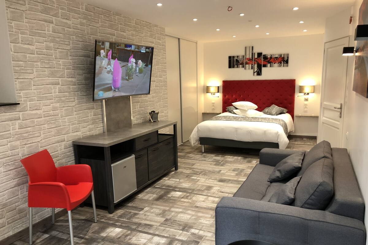 A modern hotel room with a TV, a bed, a sofa, and a red chair.