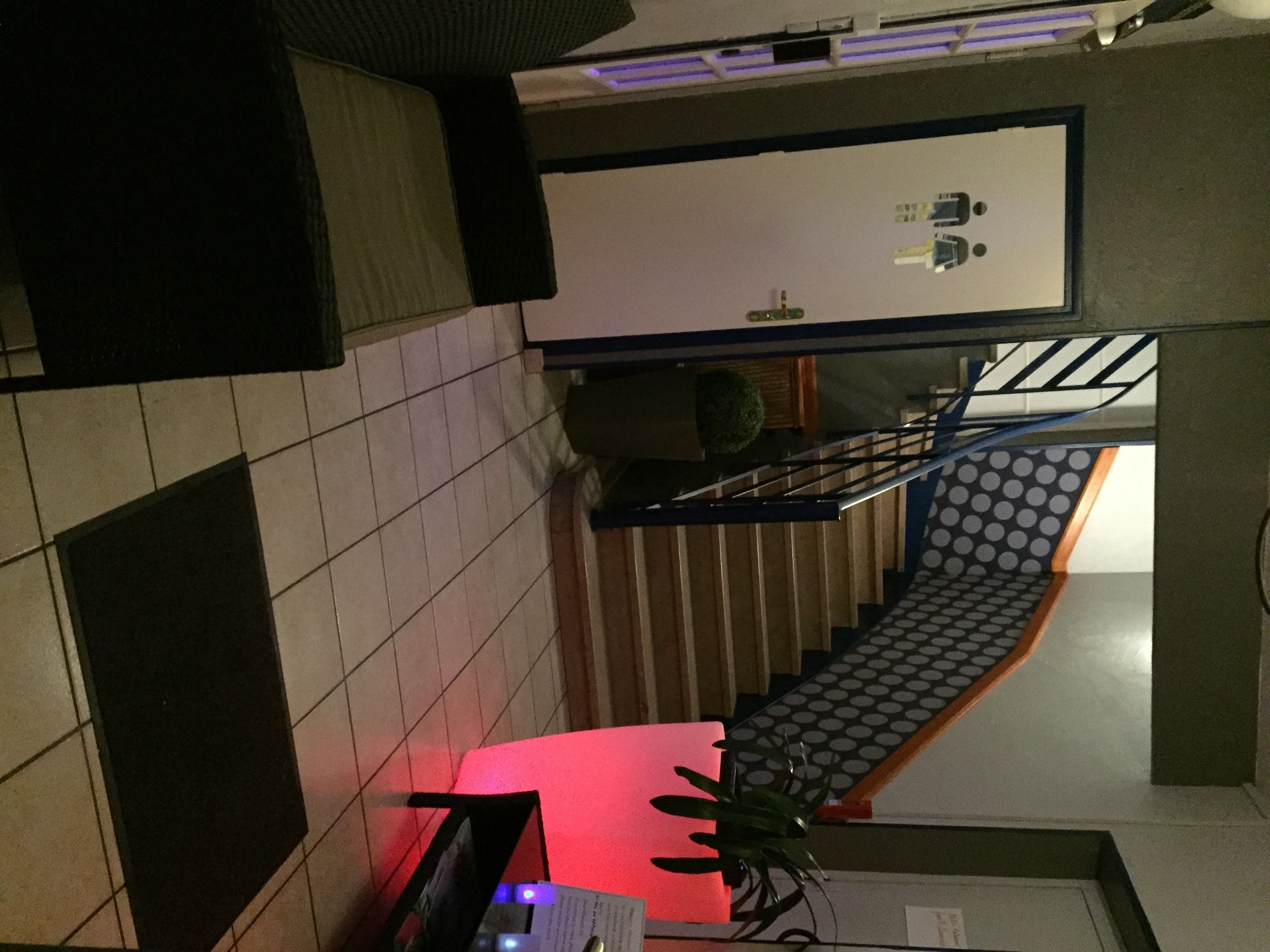 Una escalera con barandilla e iluminación roja al final, que conduce a una plataforma con una pizarra y una planta pequeña.