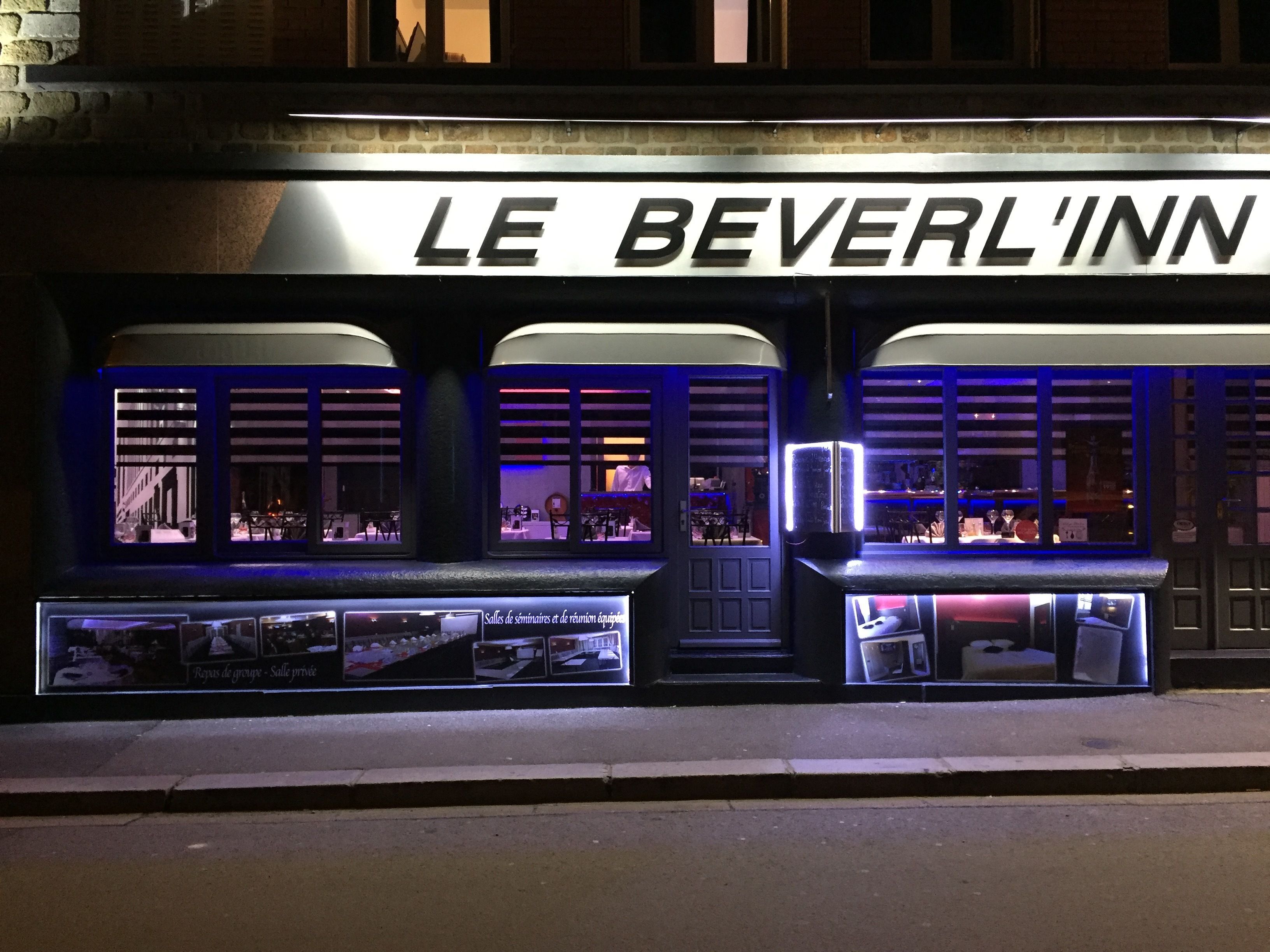 The exterior of Le Bever'l'Inn with illuminated signage and large windows displaying interior views.