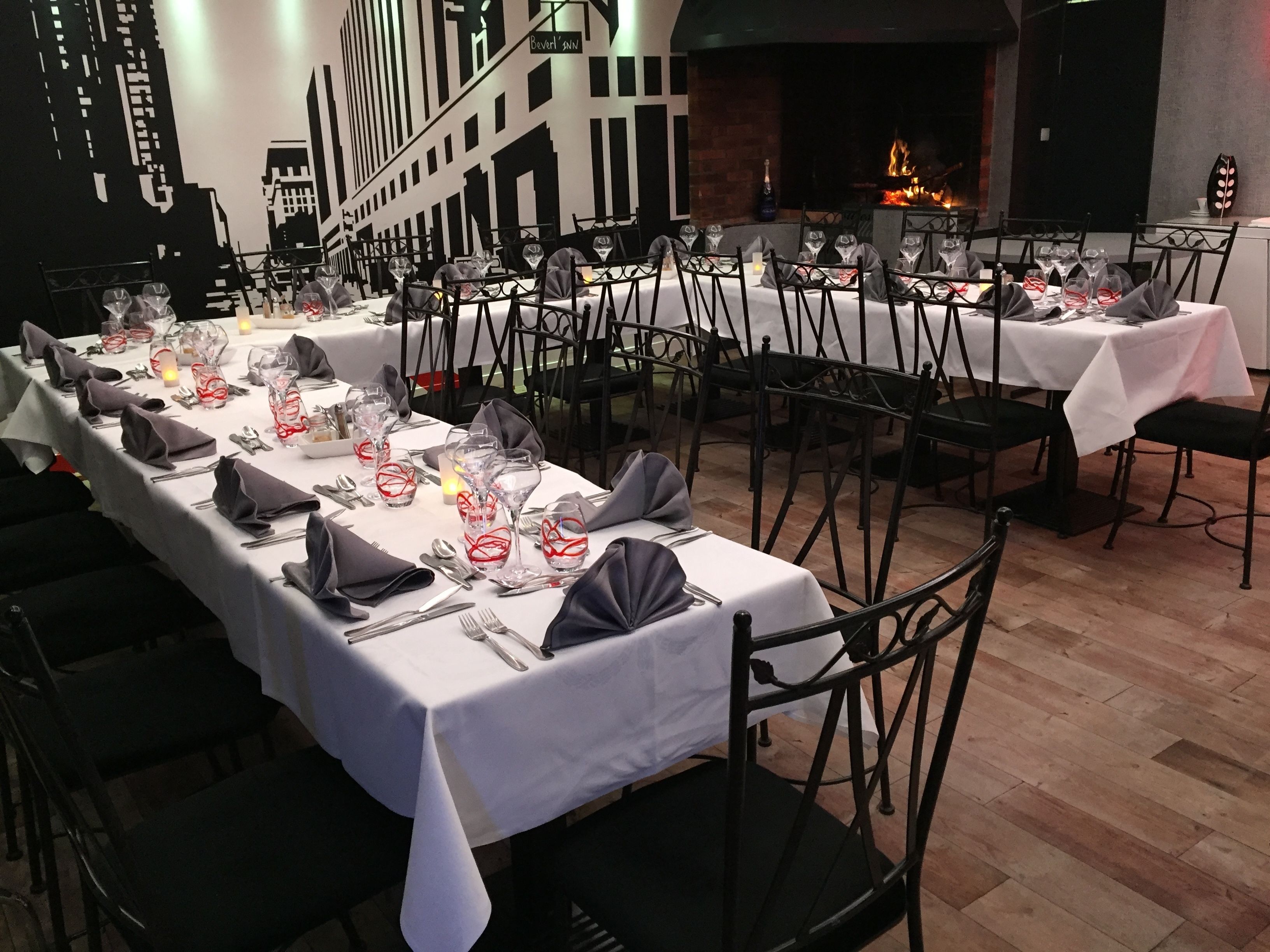 Un restaurant avec de nombreuses tables dressées pour le service, agrémenté de nappes blanches, de chaises noires et de serviettes rouges et blanches.