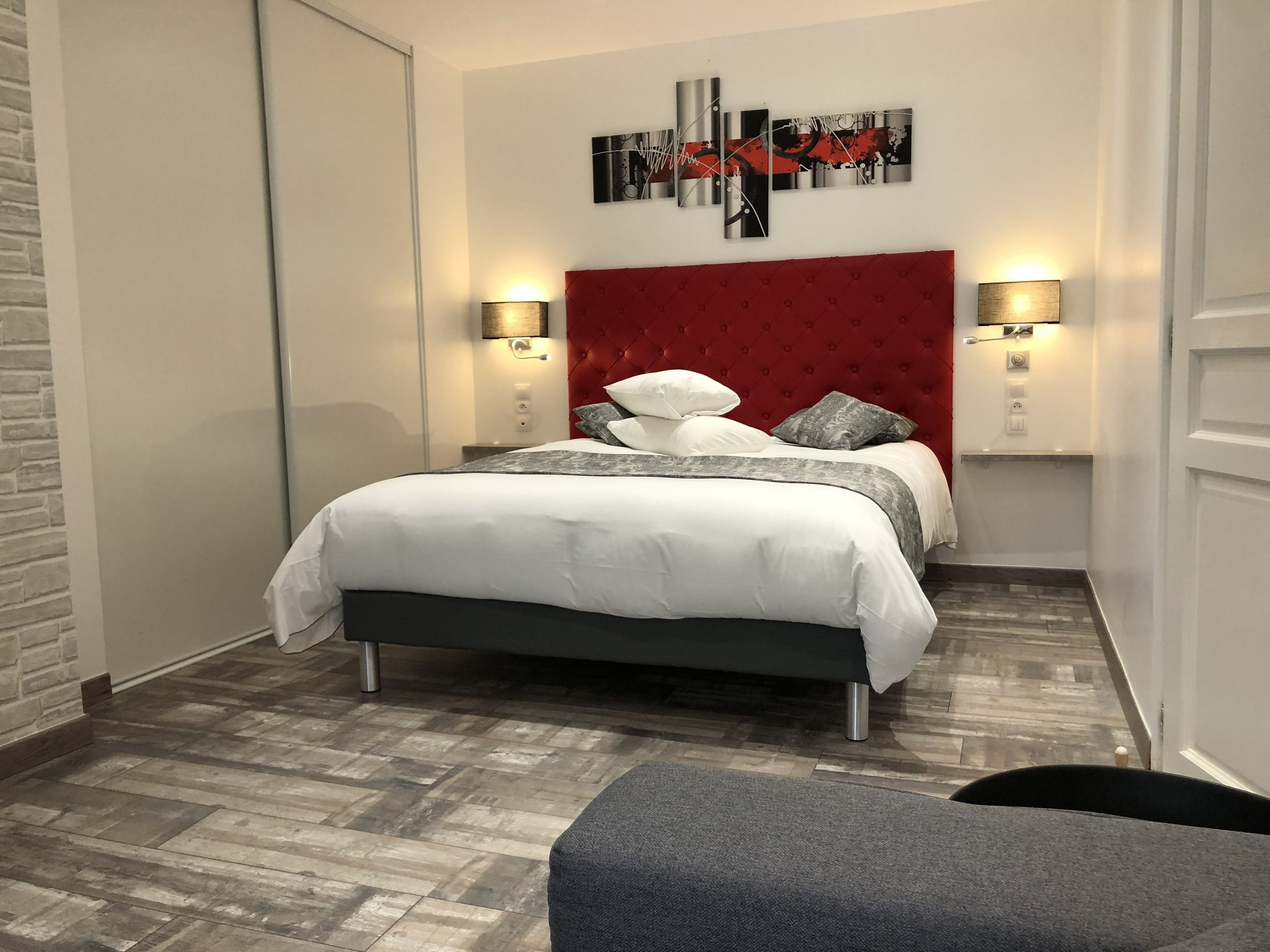 Un dormitorio moderno con una tapicería roja en la cabecera, una cama grande con ropa de cama blanca, dos lámparas de noche y una obra de arte abstracta contemporánea en la pared.