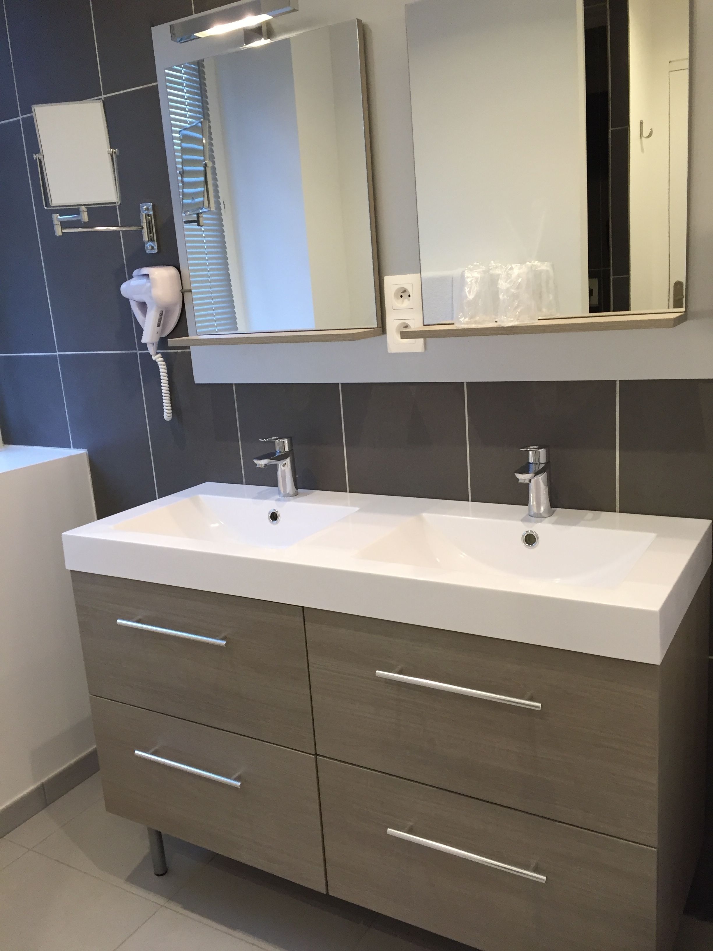A modern bathroom with a double sink vanity, a mirror above the sink, and a hairdryer on the wall.