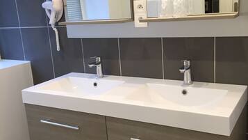 A modern bathroom with a double sink vanity, a mirror above the sink, and a hairdryer on the wall.