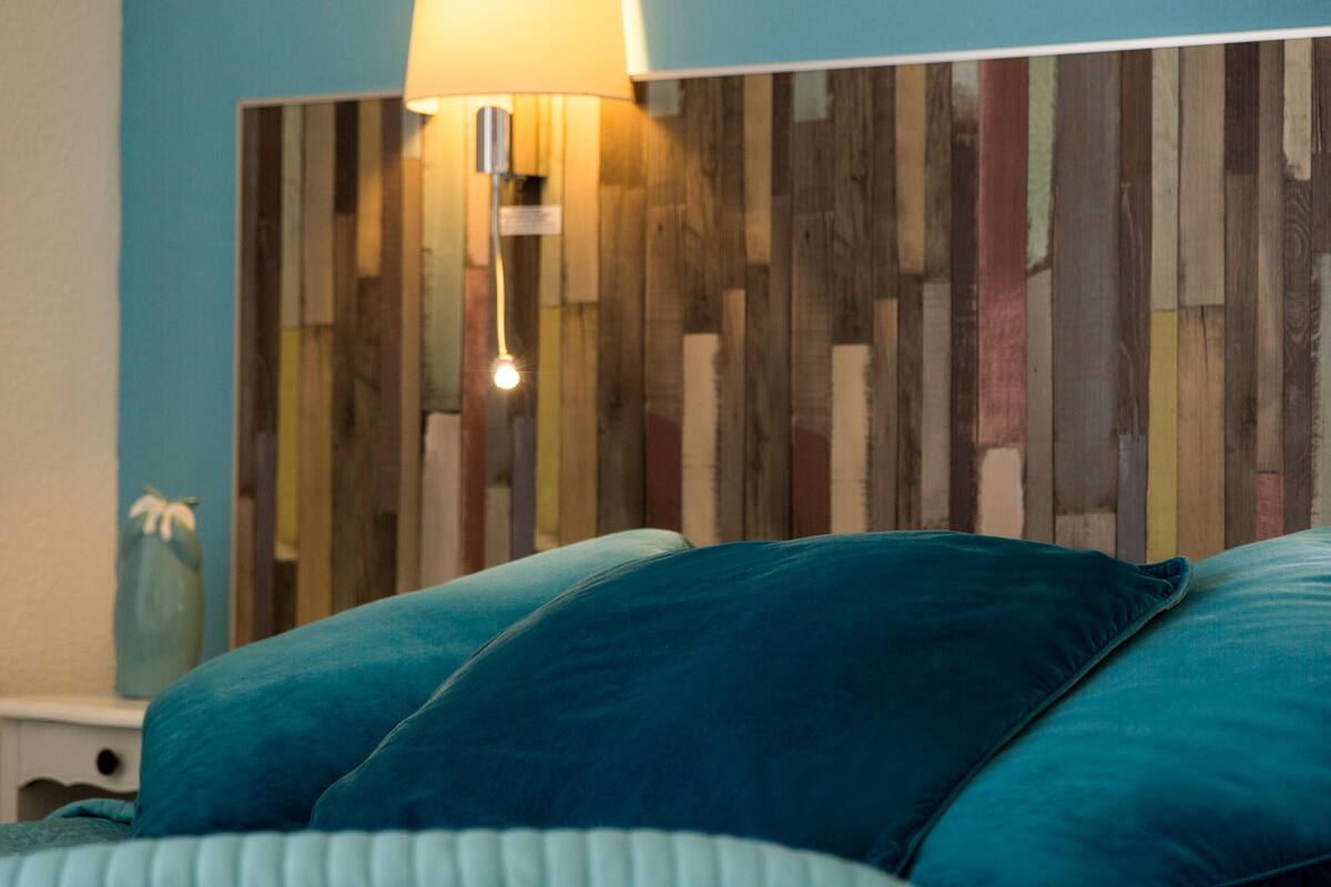 A bedroom with a wooden headboard, a bedside lamp, and teal bedding.
