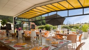 Un restaurante al aire libre con mesas preparadas para comer, un área de estar cubierta y vistas del paisaje circundante.