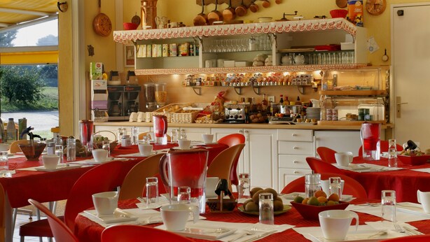 Un comedor con sillas y mesas rojas, una cocina al fondo, y diversos utensilios y electrodomésticos.