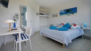 Un dormitorio con cama, escritorio, silla, televisor y un cuadro en la pared.