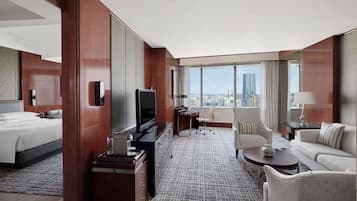 A hotel room with a bed, a desk with a computer, a TV, a sofa, and a view of the city.
