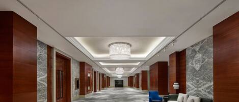 Un pasillo de hotel con candelabro, paredes de mármol y suelo alfombrado.