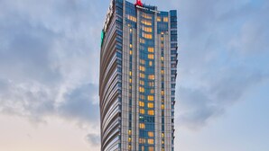 A tall, modern hotel building with a distinctive curved facade and a prominent red logo at the top. - Shanghai Marriott Marquis City Centre (Shanghai)