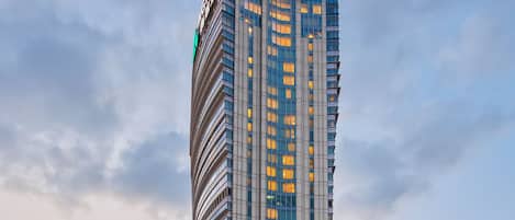 A tall, modern hotel building with a distinctive curved facade and a prominent red logo at the top.