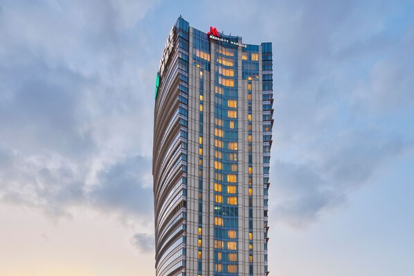 A tall, modern hotel building with a distinctive curved facade and a prominent red logo at the top. - Shanghai Marriott Marquis City Centre (Shanghai)