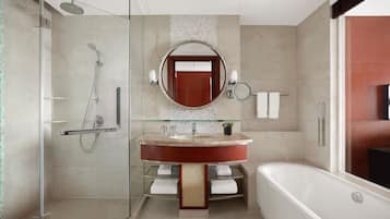 Un baño moderno con ducha envuelta en vidrio, una bañera independiente y un tocador con un espejo redondo.
