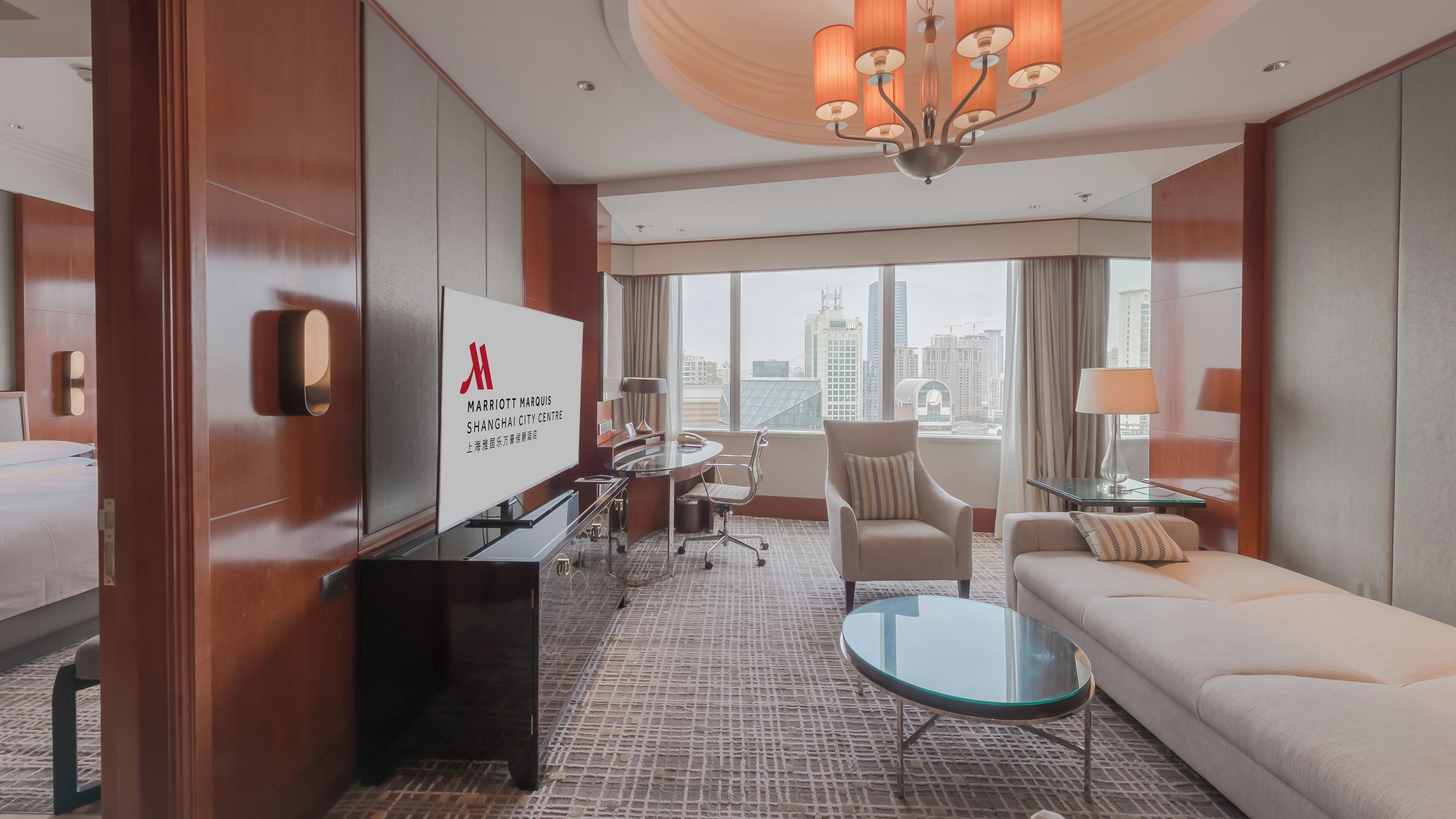 A modern hotel room with a large bed, a desk with a computer, a sofa, and a view of the city.