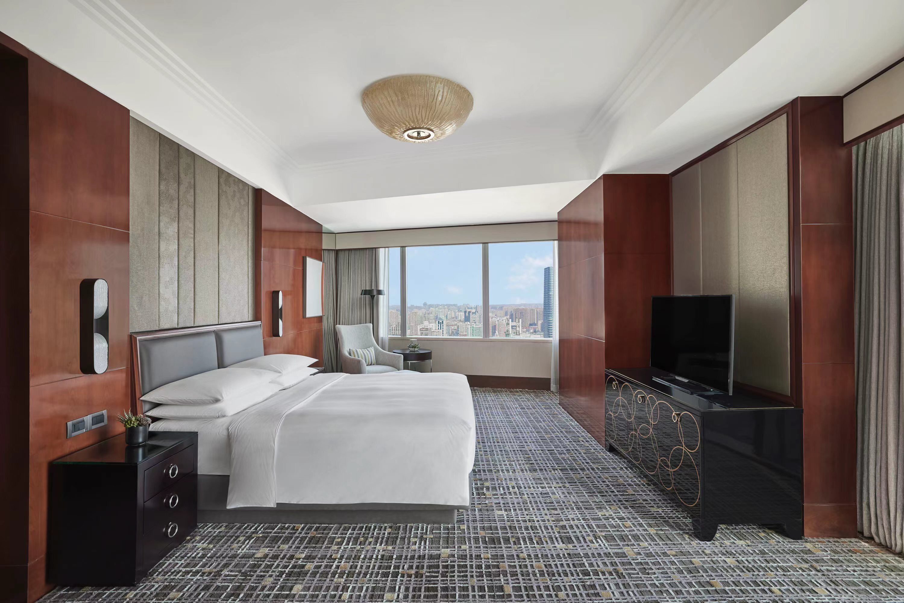 A modern hotel room with a large bed, a TV, and a city view.