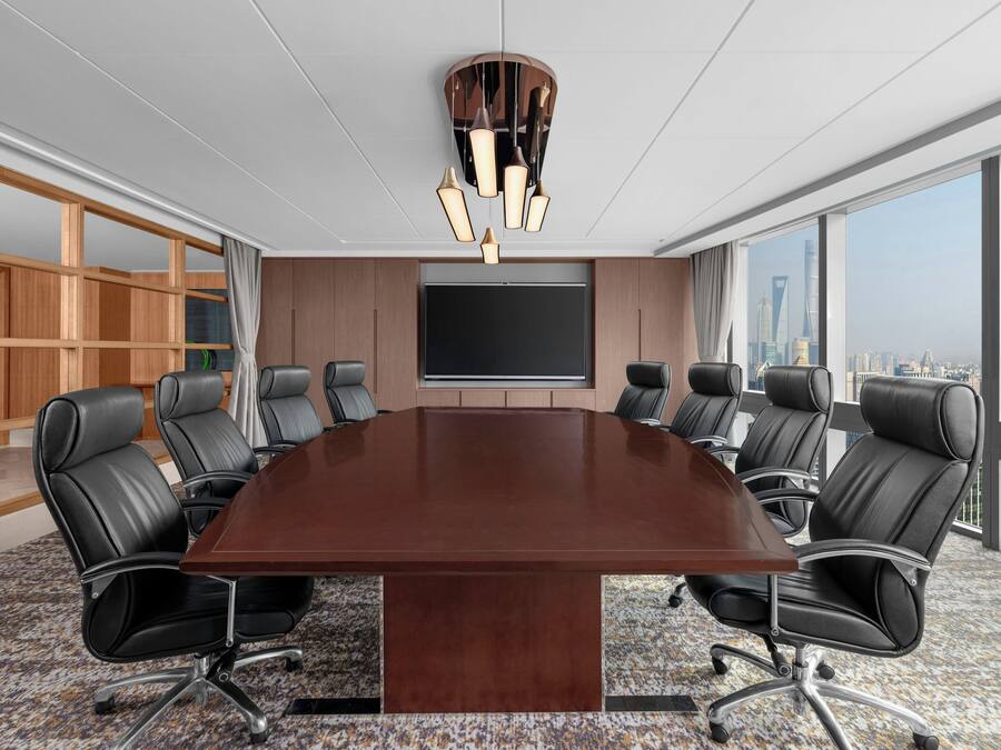 A conference room with a large table, black leather chairs, a large screen, and a city view.