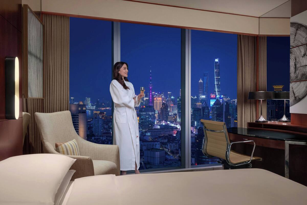 Habitación de hotel con un ventanal amplio que ofrece vistas a la ciudad, una cama, un escritorio y una silla.
