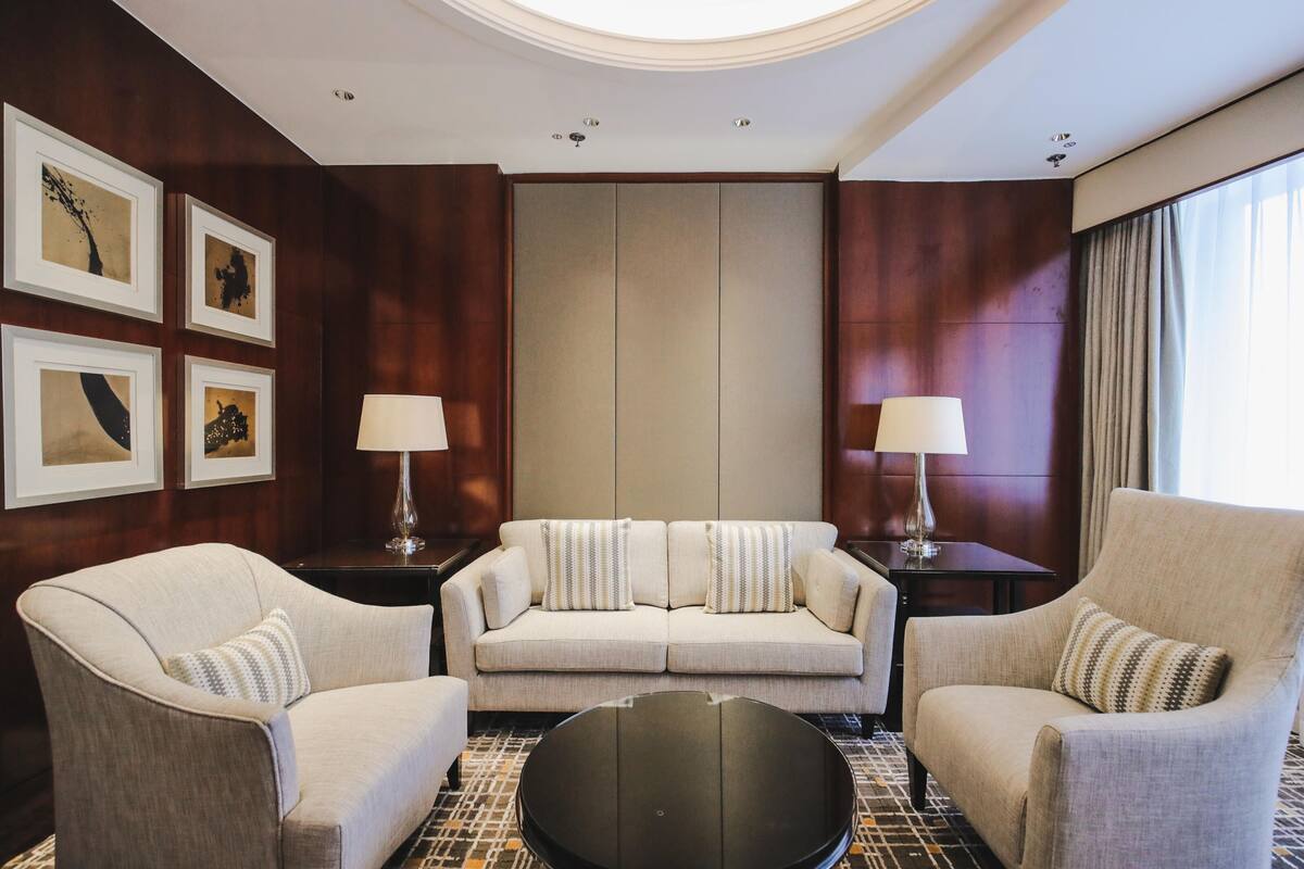 Una habitación de hotel moderna con un conjunto de sofá, dos sillones, una mesa de centro y obras de arte enmarcadas en las paredes.