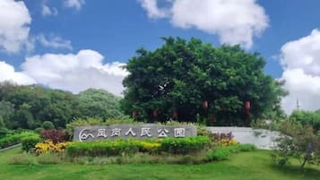 A sign with Chinese characters, a large green tree, and well-maintained grass and flowers.