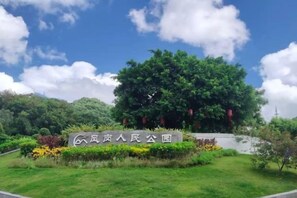 A sign with Chinese characters, a large green tree, and well-maintained grass and flowers. - Gladden Hotel (Fenggang Town) (Dongguan)