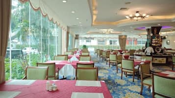 A hotel dining area with tables set for guests, large windows offering a view of the outdoors, and a ceiling with recessed lighting.