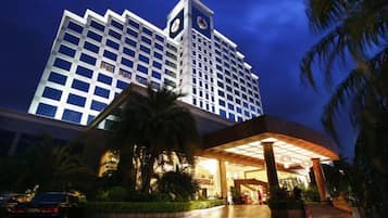 Un hotel con una imponente torre de reloj, una entrada bien iluminada y una palmera en primer plano.