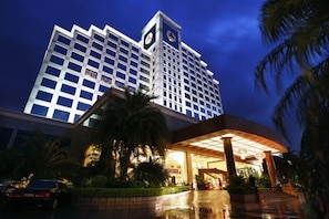 A hotel with a prominent clock tower, a well-lit entrance, and a palm tree in the foreground. - Gladden Hotel (Fenggang Town) (Dongguan)