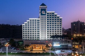 Un hotel de varios pisos con una torre destacada, estacionamiento y zona comercial.