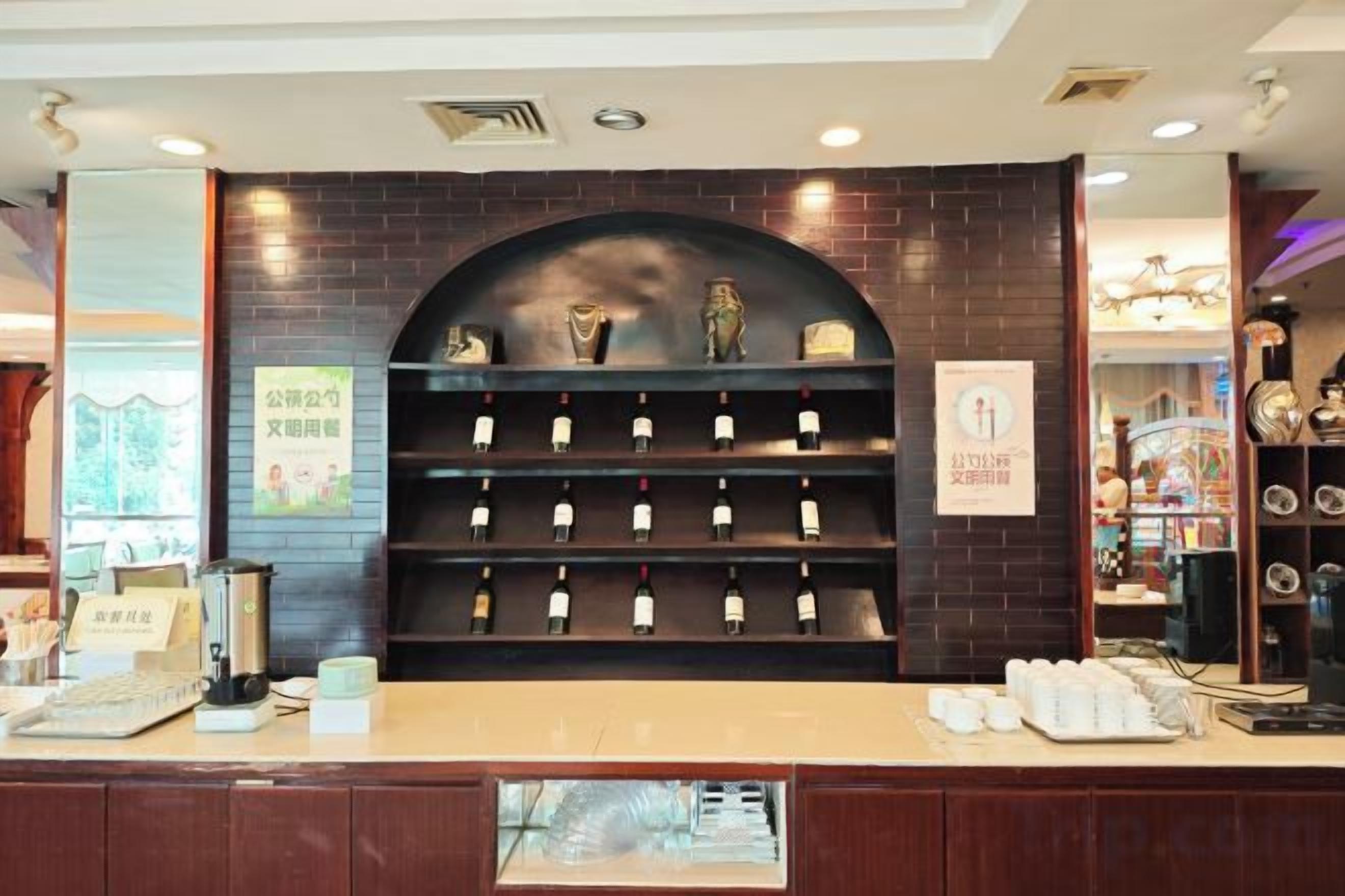 Zona de recepción con mostrador, una exhibición de botellas de vino y estante mural con objetos decorativos.