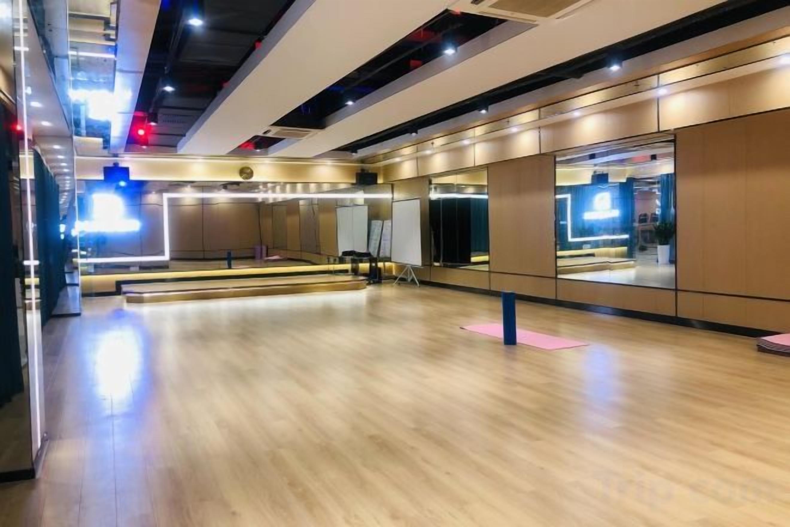 A spacious dance studio with a wooden floor, mirrors, and a large window.