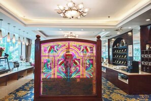 A hotel lobby with a reception desk, chandeliers, and a decorative wall with a floral pattern. - Gladden Hotel (Fenggang Town) (Dongguan)